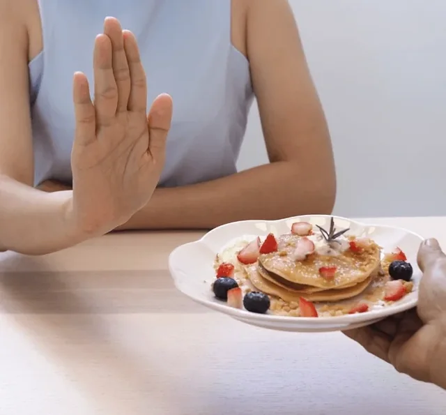 A hand held up to refuse a plate of pancakes with berries, a lifestyle picture from the seller's image set