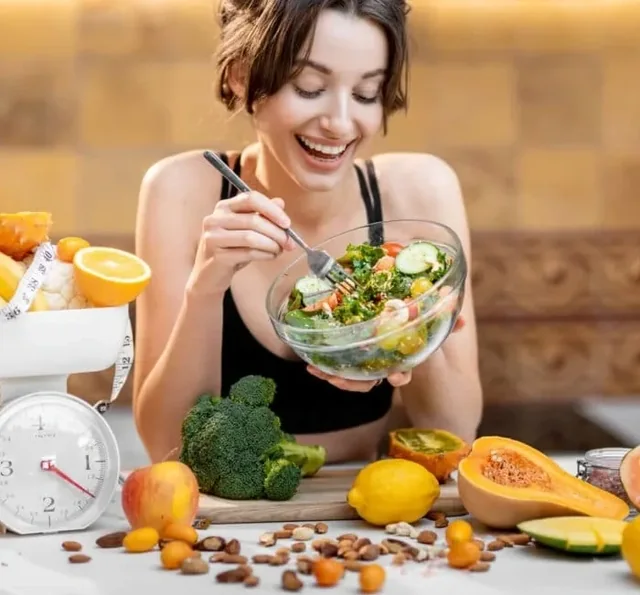A smiling woman eating a salad at a kitchen table, a lifestyle picture from the seller's image set